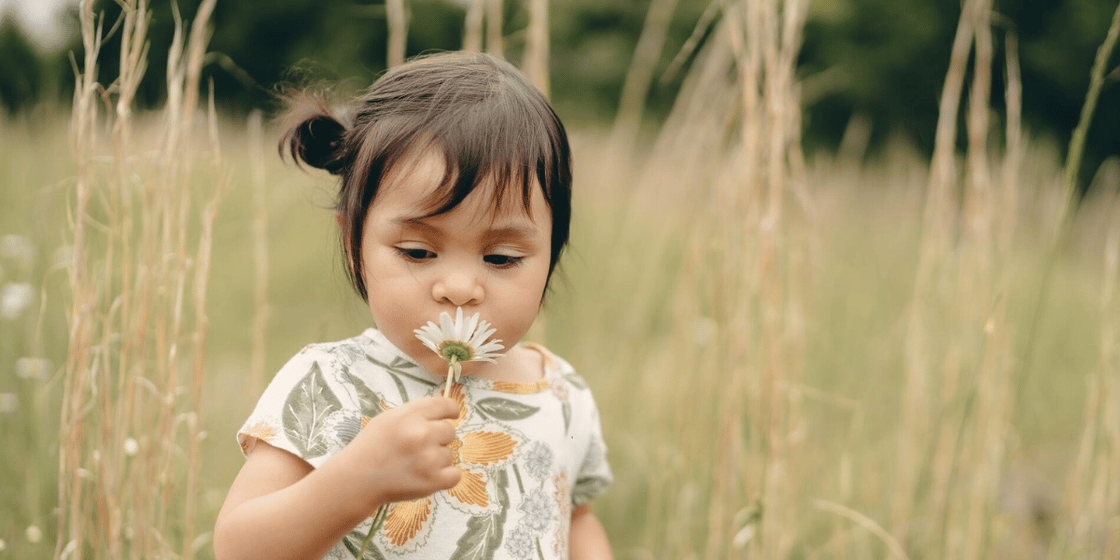young child holding a wildflower up to their nose in vast field