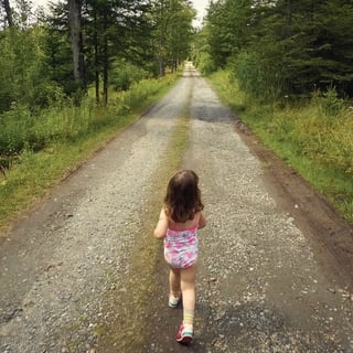 young child walking alone on gravel path in forest